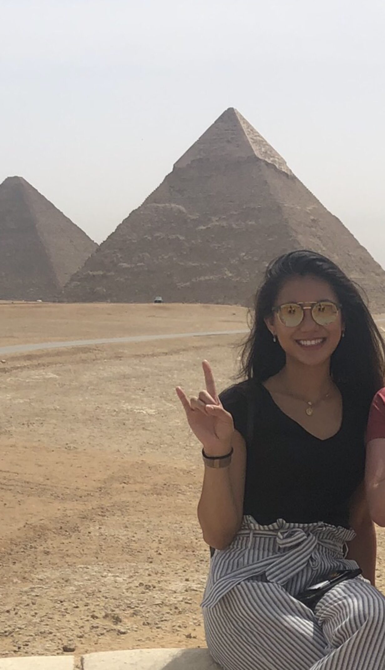 woman wearing glasses holds up hand sign near pyramids