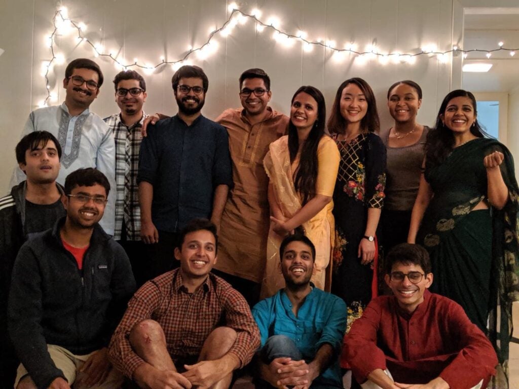 large group of people dressed in traditional indian garb pose in front of wall with fairy lights