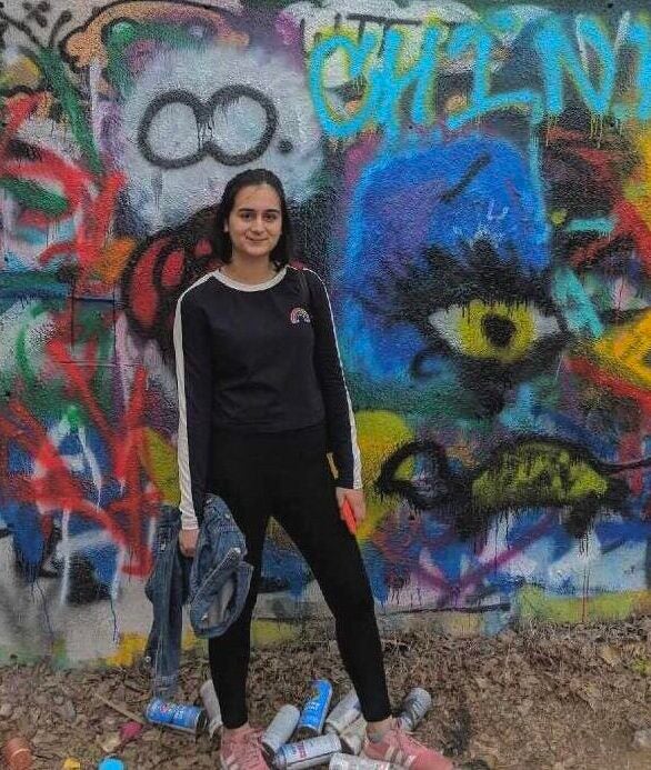 Fatima stands in front of a graffitied wall