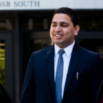 three people in suits talk in front of the mccombs building