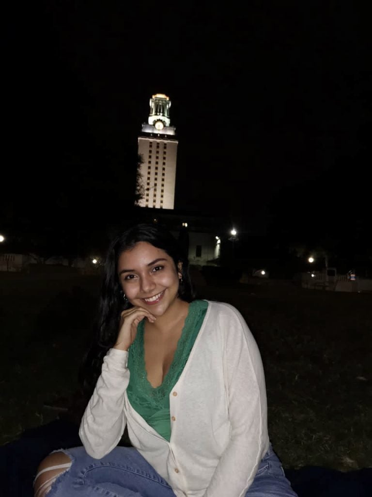 Abrego smiles and poses near the illuminated UT tower during nighttime