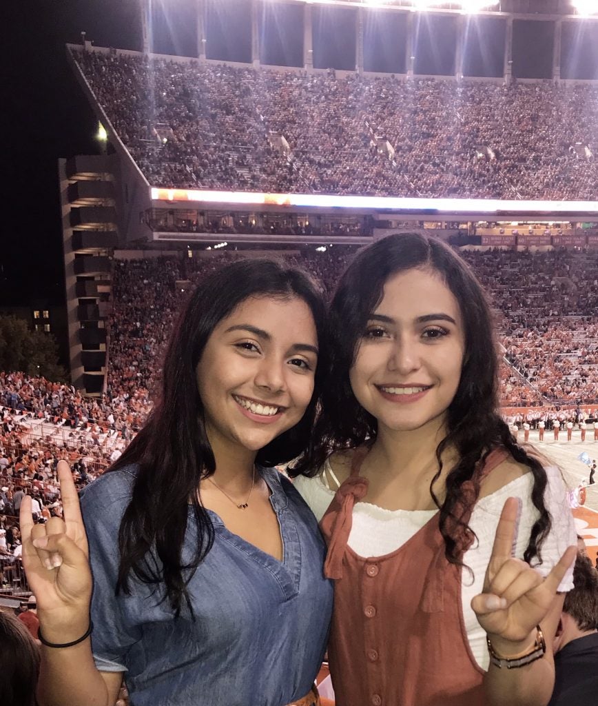 Abrego smiles with friend and puts up hook'em horns hand signs in crowded UT stadium