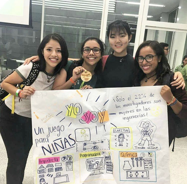 four students hold up hand drawn poster in classroom 