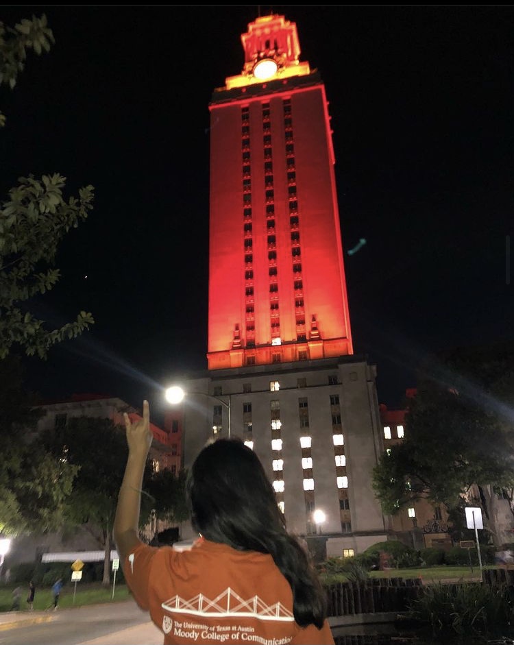 woman wearing orange faces away and throws up hand sign near orange-lit tower