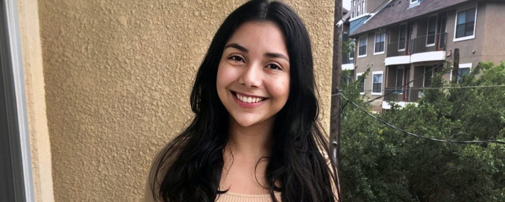 Clarissa smiles in front of a beige wall