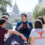 UT students sit and discuss in a small group. The capitol and front lawn are in the background.