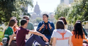 UT students sit and discuss in a small group. The capitol and front lawn are in the background.
