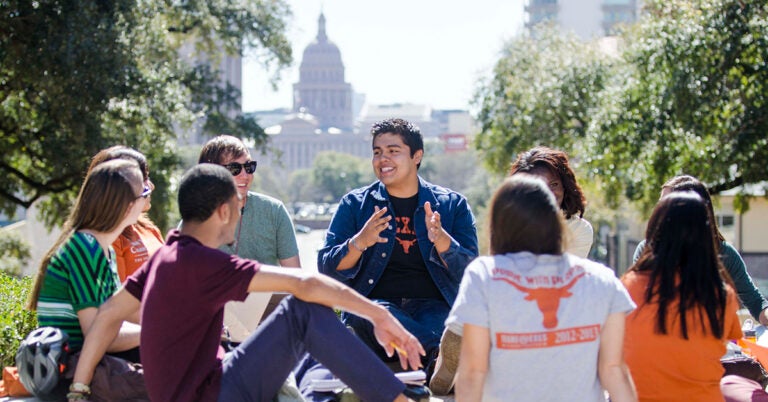 UT students sit and discuss in a small group. The capitol and front lawn are in the background.