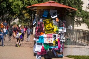 A kiosk on UT campus holds many colorful flyers advertising student events.