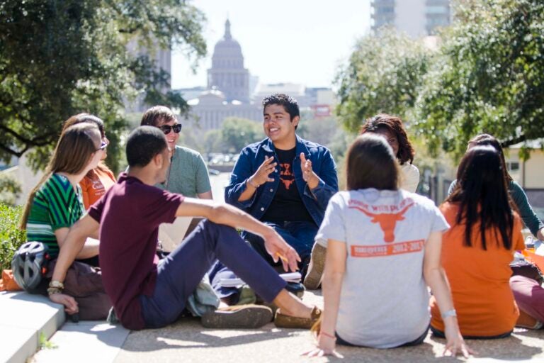 Students sit in a circle on the South Mall with the Texas capitol behind them
