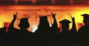 ISSS grads look towards the illuminated UT main building while showing the hook'em sign in their graduation gowns
