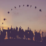 Student toss their graduation hats in the air in a perfect arch. The sun sets behind them