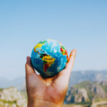 Image of a single hand holding a small globe with a mountain landscape in the background.