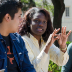 A group of four students sit outside of the University of Texas at Austin in mid conversation.