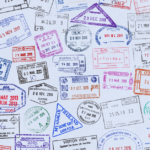 A blank sheet of paper filled up with many different visa and immigration stamps from various countries. Some stamps in the shape of a circle, others in a square or triangle.