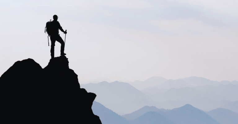 A solo-hiker climbs a mountain and overlooks the vast range of smaller mountains in the distance