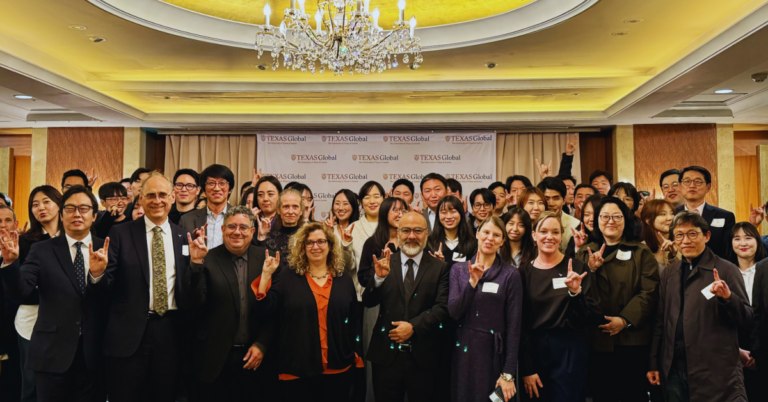 several adults in black and dark colored suits smile at the camera while in a ball room
