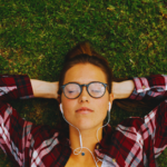 Woman in a plaid shirt and glasses lays on the lawn in relief