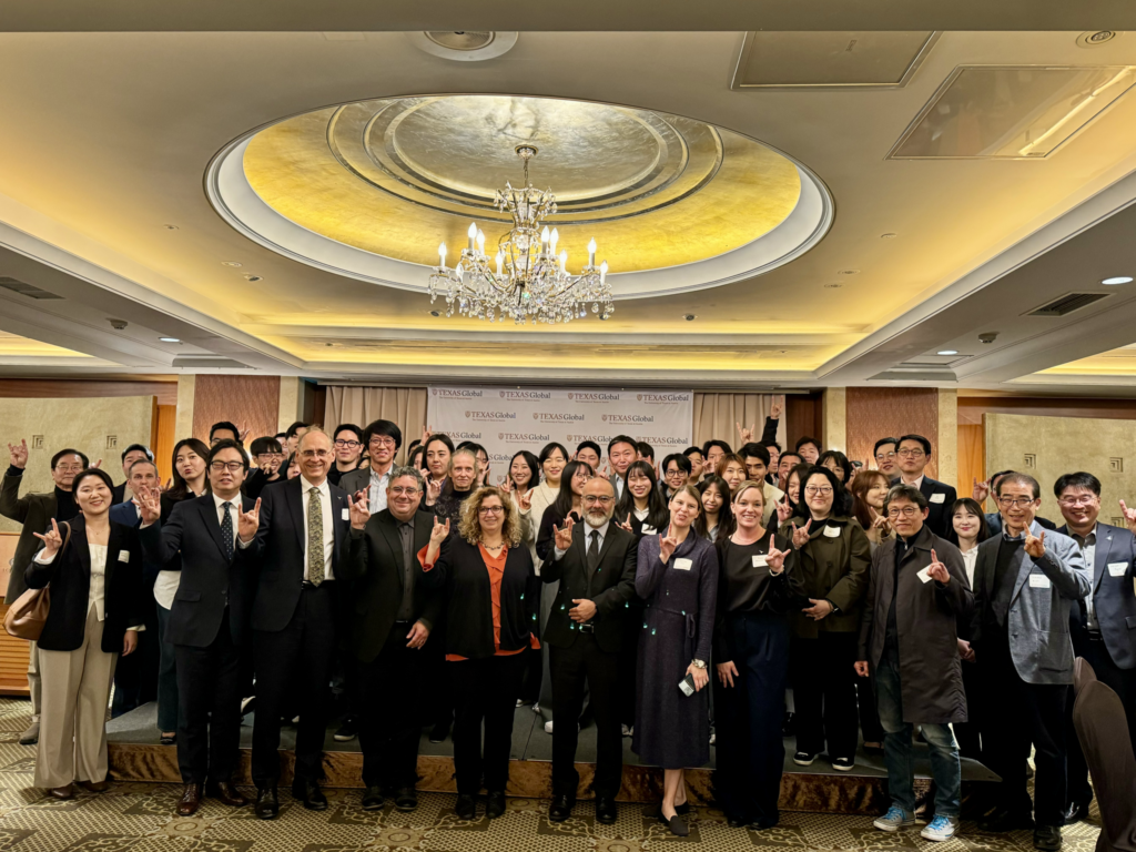 Several adults in black and dark colored suits smile at the camera while in a ball room