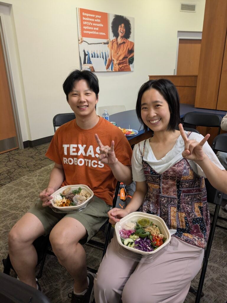 Two students eating food and signaling Hook Em'