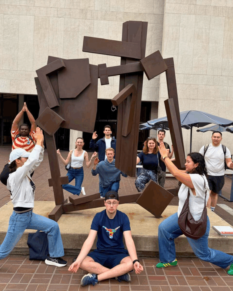 Students together doing poses near a statue/art piece in front of the PCL