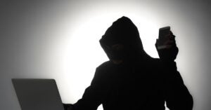 Hacker/Scammer in front of laptop holding a cellphone