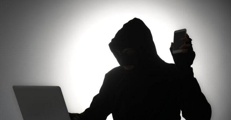 Hacker/Scammer in front of laptop holding a cellphone