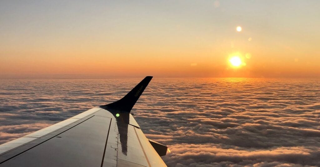 Airplane wing in foreground against a backdrop of dense, fluffy clouds at sunset; warm orange and golden sky conveying peace and serenity.