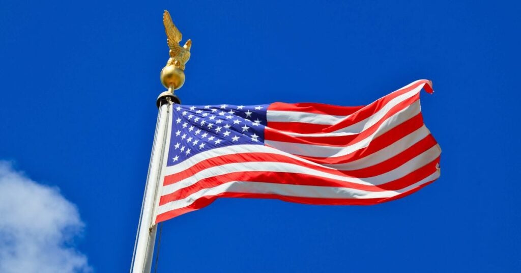 American flag waving against a clear blue sky with a golden eagle finial on the flagpole.