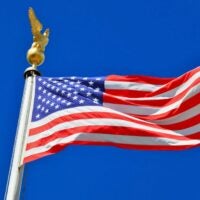 American flag waving against a clear blue sky with a golden eagle finial on the flagpole.