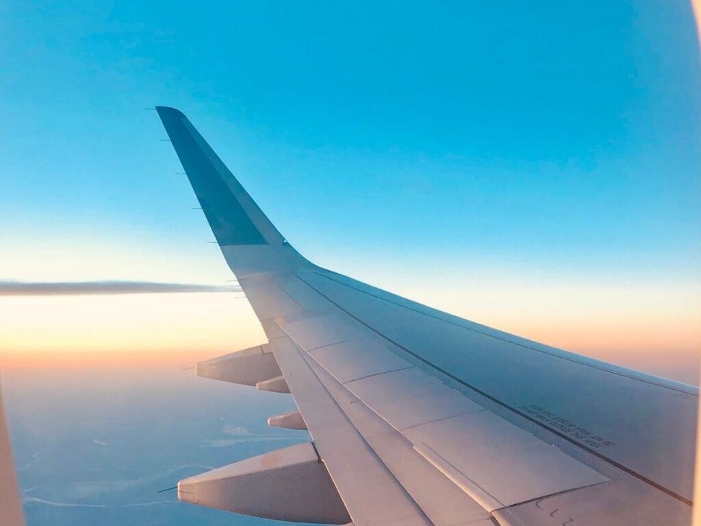 View of an airplane wing against a clear sky during sunset from the passenger window.