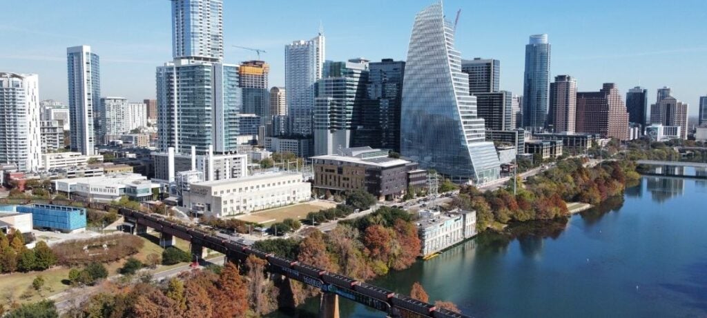 Aerial view of Austin's skyline with diverse skyscrapers along a riverbank lined with autumn trees.