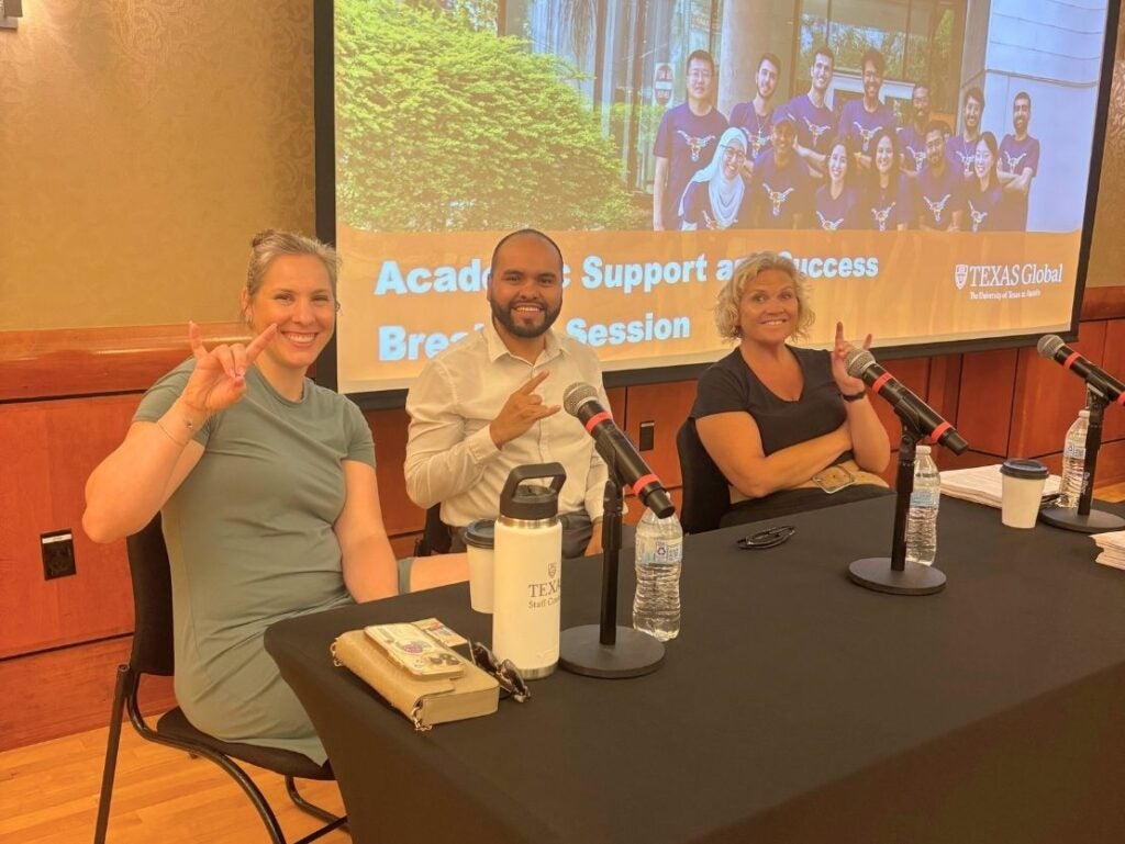 Three people seated at a table with microphones, smiling and making hand gestures during a Texas Global academic support session.